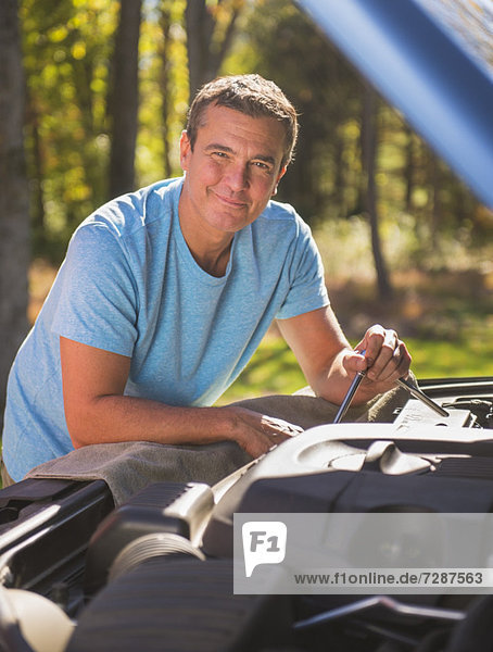 Man leaning on car with hood open at roadside