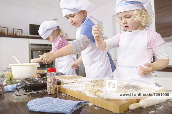 Germany  Girls and boy baking cup cakes and pouring sugar sprinkles