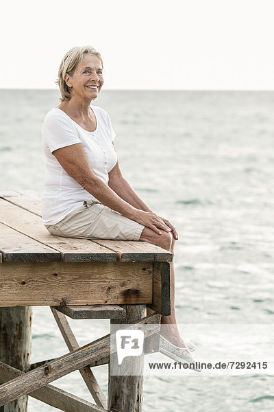 Spain,  Senior woman sitting on jetty at the sea