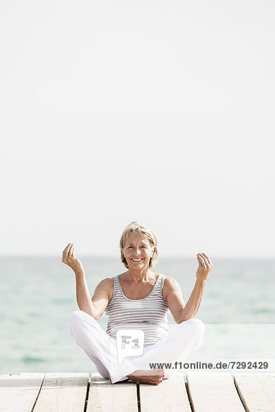 Spain,  Senior woman doing yoga on jetty at the sea