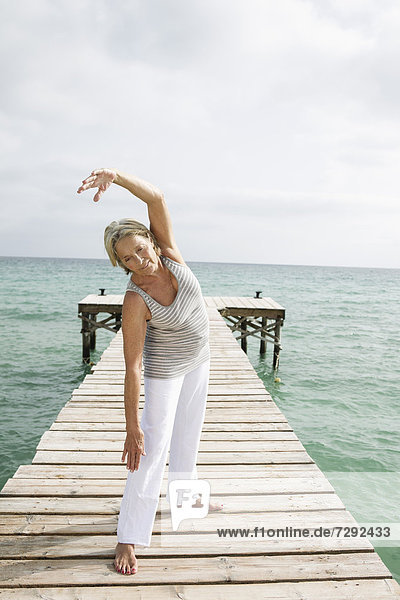 Spain  Senior woman doing yoga on jetty at the sea