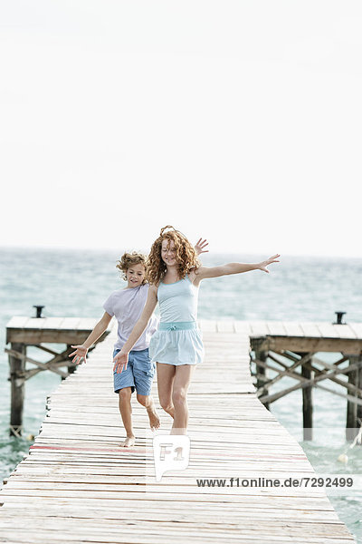 Spain  Girl and boy running on jetty at he sea