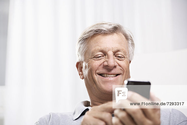 Spain,  Senior man checking emails on mobile,  smiling