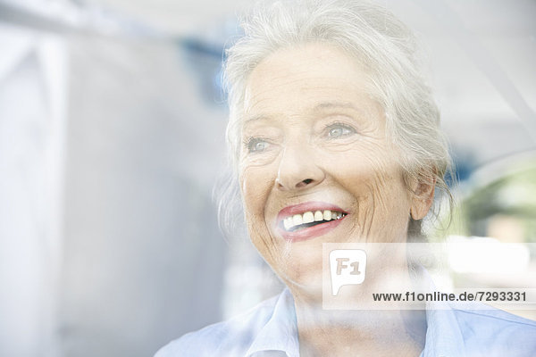 Spain  Senior woman looking through window  smiling