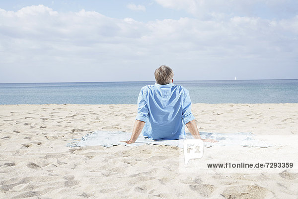 Spanien  Senior am Strand sitzend