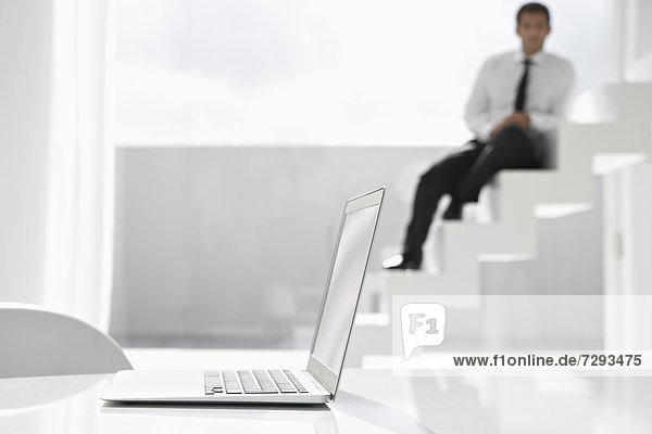 Spain  Businessman sitting on stairs  laptop in foreground
