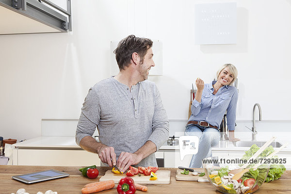 Mature man chopping vegetables  woman sitting in background