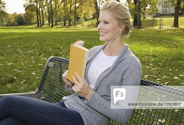 Europe  Germany  North Rhine Westphalia  Duesseldorf  Young woman reading book on park bench