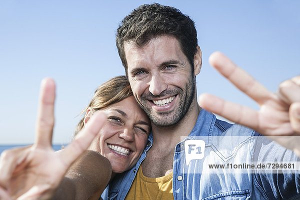 Spanien  Mittleres erwachsenes Paar mit Friedenszeichen  lächelnd  Portrait
