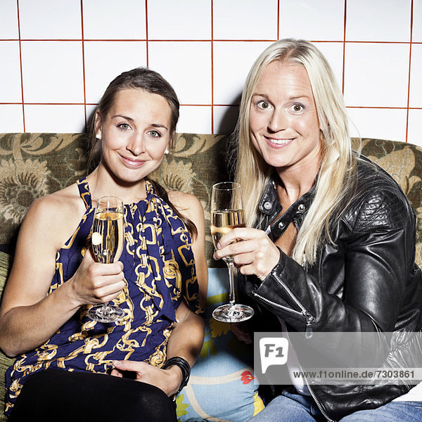 Portrait of happy female friends holding champagne flutes on sofa