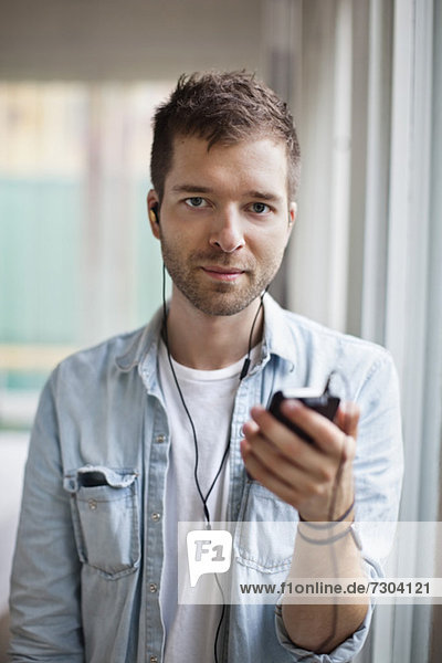 Porträt eines jungen Mannes  der Musik über das Handy hört.