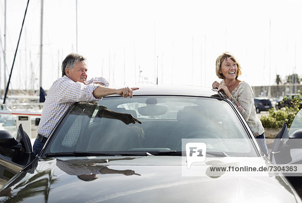 Älterer Mann  der der Frau etwas zeigt  während er sich auf das Auto stützt.