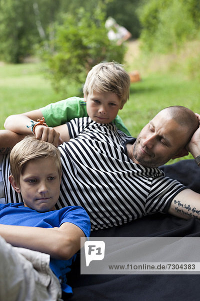 Erwachsener Mann mit Söhnen  die auf Gras im Park liegen