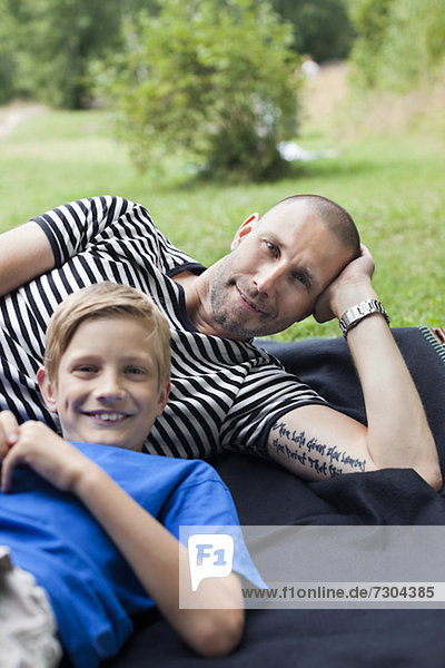 Portrait of mature man and son lying on grass at park