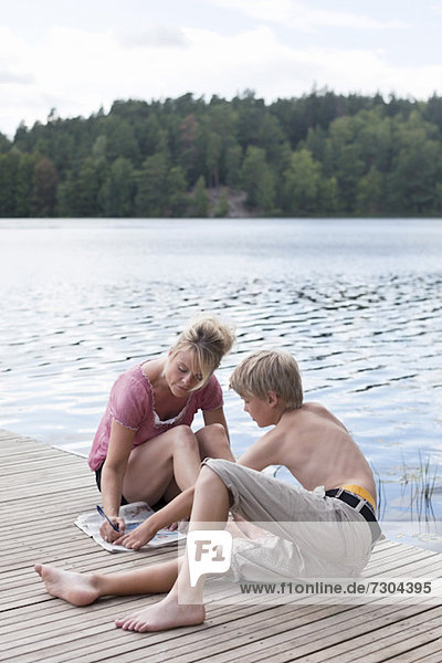 Mature woman writing on newspaper sitting with son on pier