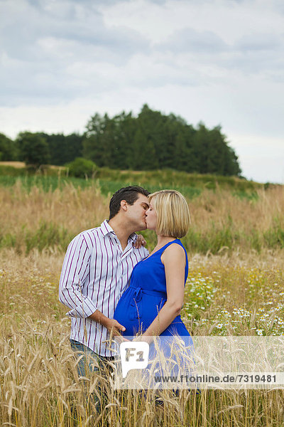Mann und schwangere Frau küssen sich in einem Feld