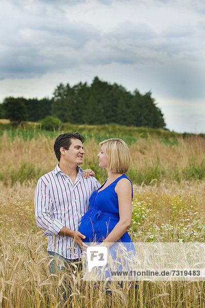 Mann und schwangere Frau umarmen sich in einem Feld