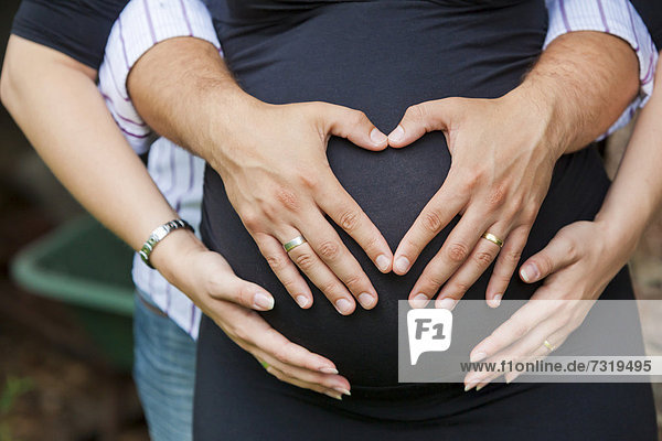 Mann und schwangere Frau formen mit ihren Händen ein Herz auf ihrem Babybauch
