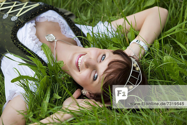 Junge Frau im Dirndl und mit Hopfenkrone liegt im Gras  Hopfenvizekönigin der Hallertau  Holledau oder Hollerdau  Bayern  Deutschland  Europa