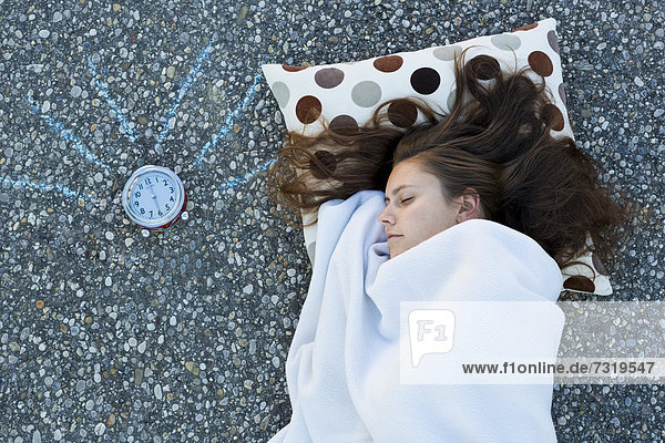 Junge Frau liegt mit Kissen und Decke am Boden  der Wecker klingelt  von oben aufgenommen