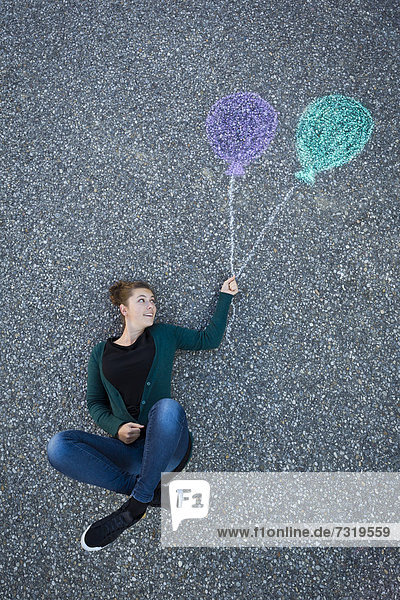 Junge Frau scheint an zwei gemalten Luftballons zu hängen  von oben aufgenommen