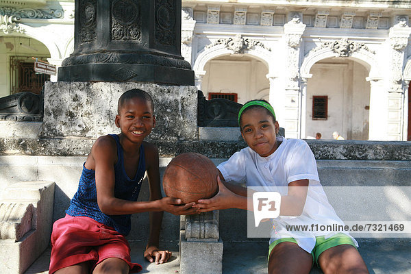 Zwei Jungs mit einem Basketball auf einer Bank in der Paseo de Marti Straße  Havanna  Kuba  Amerika