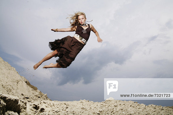 Frau springt von einem Sandhügel