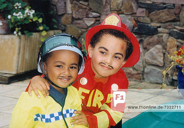 Children outdoors in garden. Two boys dressed-up as firefighter and policeman.