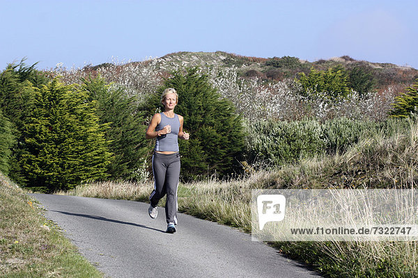 Blonde woman outdoors. Jogging along country road.