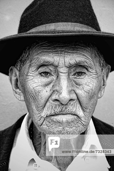 Local black and white image of old man with wrinkles and great eyes against bright wall with black cowboy hat in tourist village of Antigua Guatemala