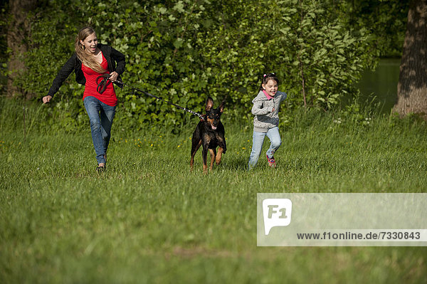 Two girls running with a Doberman across a meadow