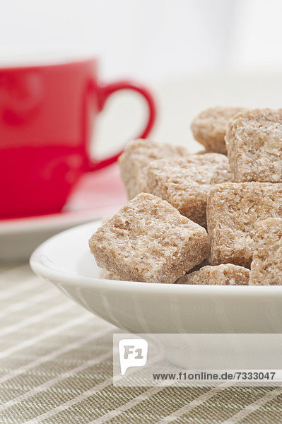 Brauner Würfelzucker und eine rote Kaffeetasse