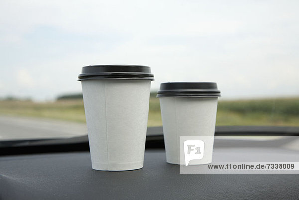 Zwei Einwegbecher Kaffee auf dem Armaturenbrett eines Autos
