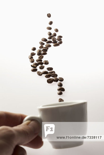 Ein Mann hält eine Kaffeetasse mit darüber schwebenden Kaffeebohnen.