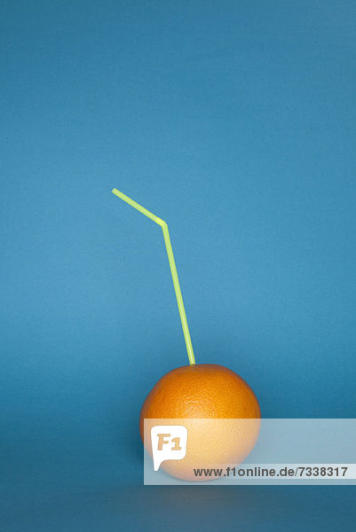 An orange with a drinking straw stuck in it
