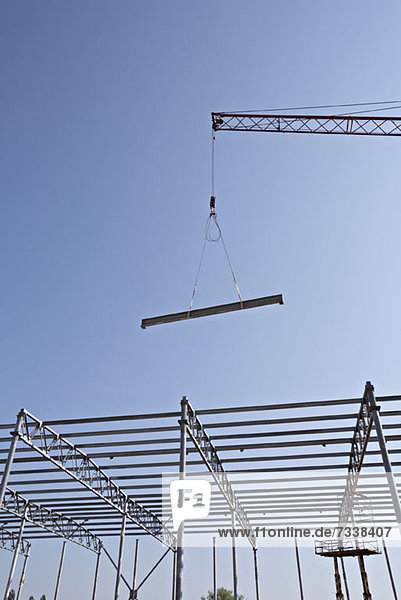 Crane lowering steel beam towards construction frame