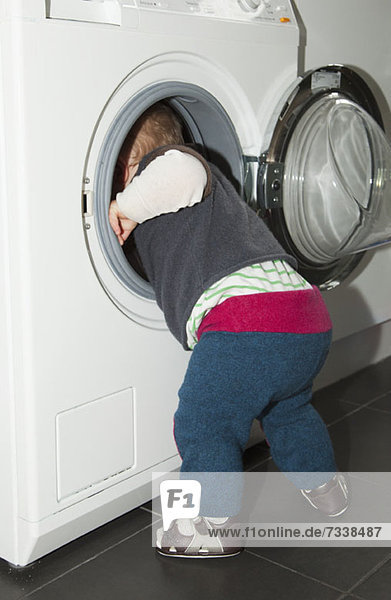Ein kleiner Junge  der in eine Waschmaschine greift.