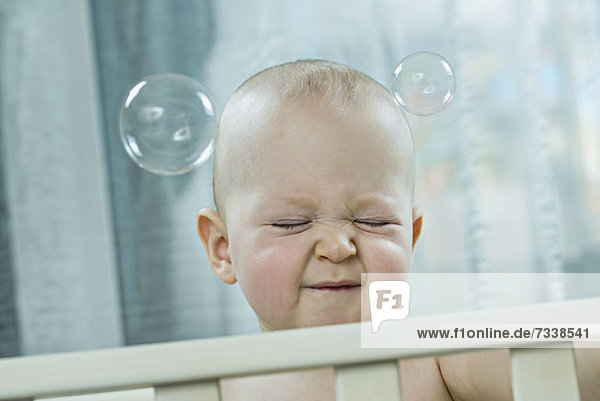 Baby drückt die Augen zu  wenn Blasen an seinem Kopf vorbeiziehen.