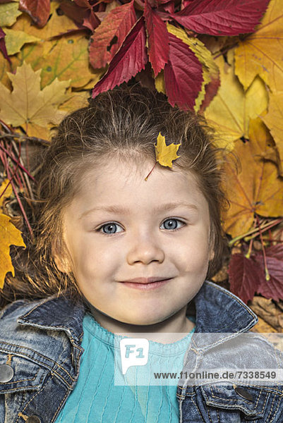 Ein junges Mädchen liegt zwischen Herbstblättern.