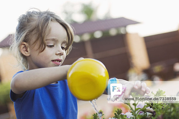 Ein junges Mädchen  das eine Blume mit einer Spielzeug-Gießkanne gießt.