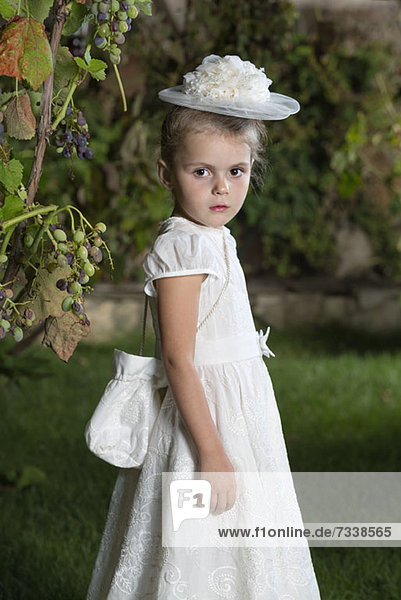Ein junges Mädchen  elegant gekleidet in weißem Kleid  Hut und Geldbörse.