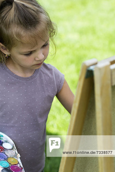 Ein junges Mädchen konzentriert sich ernsthaft  während sie auf einer Staffelei malt.