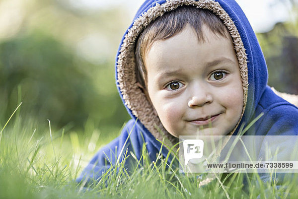 Ein kleiner Junge mit Kapuzenjacke im Gras