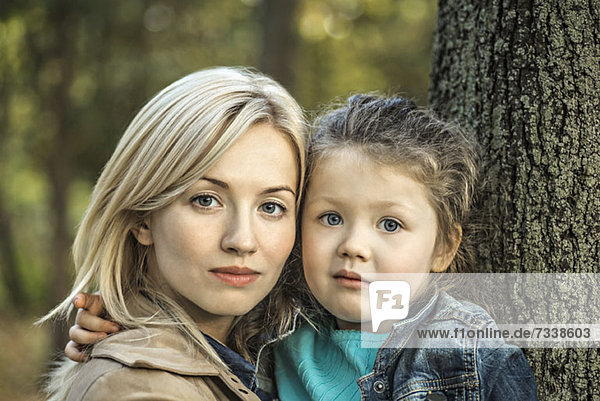 Eine heiter aussehende Mutter und ihre kleine Tochter neben einem Baumstamm
