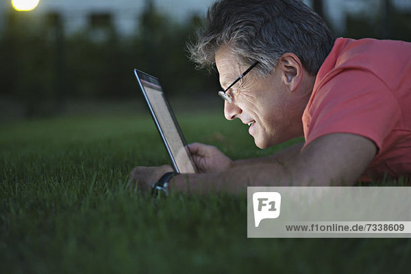 A mature man lying in the grass using a laptop