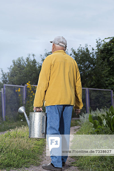A senior man carrying a metal water can in his backyard