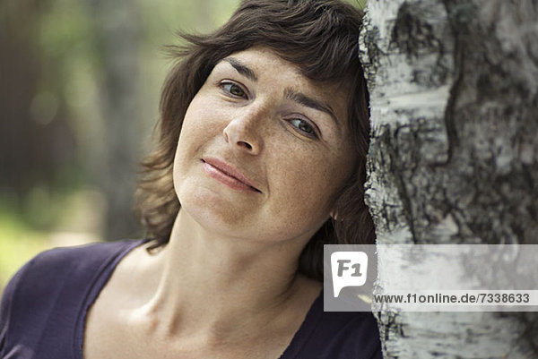Eine ruhige Frau  die sich an einen Baumstamm lehnt.