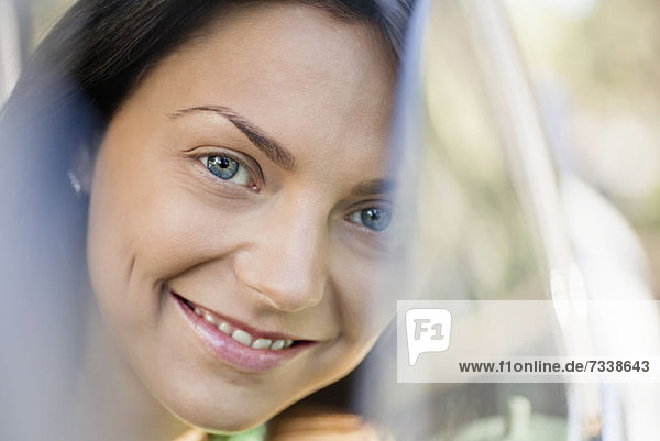 Eine schöne junge Frau lächelt  während sie durch ein Autofenster schaut.