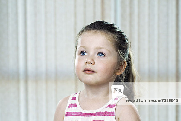 A young girl wearing a striped tank top and looking up thoughtfully