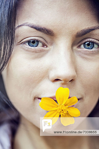 Eine junge Frau  die eine gelbe Blume in ihrem Mund hält.